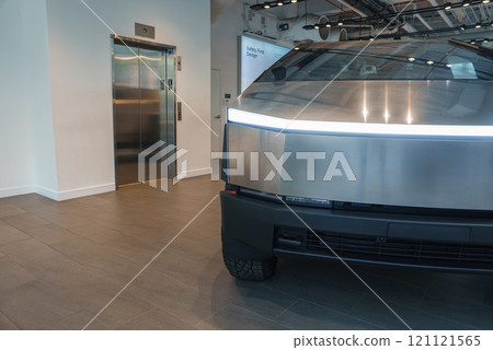 A futuristic vehicle with angular design and metallic finish is showcased indoors. The setting includes tiled flooring and an elevator, suggesting a showroom. 121121565