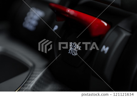 The image captures a close up of a red start or stop engine button in a luxury car interior, featuring carbon fiber detailing and gear options 'P' and 'M'. The image captures a close up of a red start or stop engine button in a luxury car interior, featuring carbon fiber detailing and gear options 'P' and 'M'. 121121634