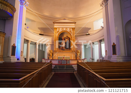 The neoclassical altar area of Helsinki Cathedral features an ornate altarpiece, classical columns, and statues, with white walls and gold accents. 121121715