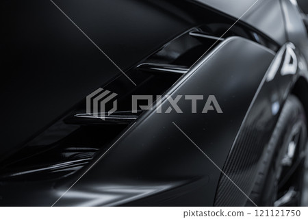 The image features a close up of a black McLaren 720S, focusing on its aerodynamic design, prominent air vents, and glossy surfaces reflecting light. 121121750