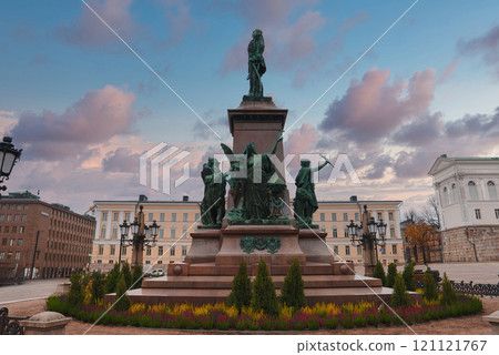 The statue of Alexander II stands in Senate Square, Helsinki, with the Helsinki Cathedral partially visible. A vibrant sky with clouds forms the backdrop. 121121767