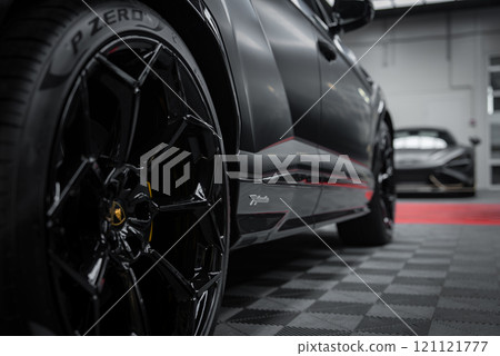 A close up view of a Lamborghini Urus Performante's sleek black exterior and Pirelli P Zero tires, with a McLaren 720S partially visible in an indoor showroom. 121121777