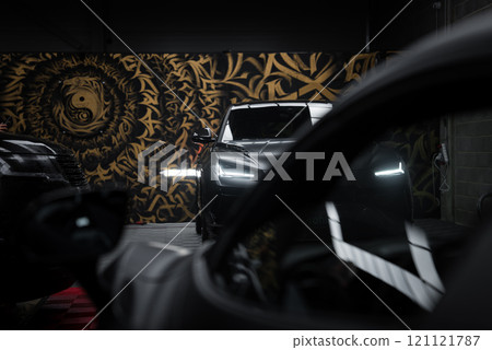 A luxury Lamborghini Urus Performante with illuminated headlights in a garage. A gold and black mural and a McLaren 720S reflection enhance the scene. 121121787