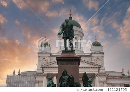 Helsinki Cathedral's neoclassical architecture with green domes is set against a sunset sky. The Alexander II statue stands prominently in the foreground. Helsinki Cathedral's neoclassical architecture with green domes is set against a sunset sky. The Alexander II statue stands prominently in the foreground. 121121795