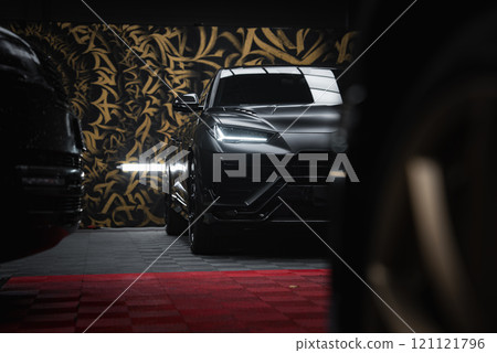 A close up view of a Lamborghini Urus Performante indoors, with gold and black patterns in the backdrop. Red and black checkered flooring is visible. A close up view of a Lamborghini Urus Performante indoors, with gold and black patterns in the backdrop. Red and black checkered flooring is visible. 121121796