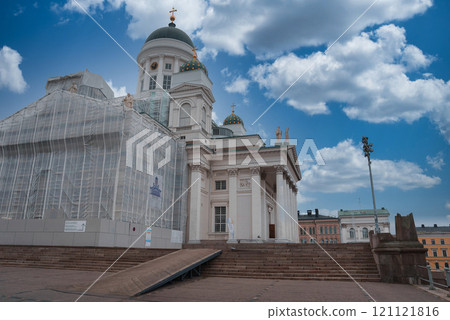 Helsinki Cathedral's neoclassical architecture stands out with its white facade and green domes. Scaffolding is present, and the sky is clear with clouds. 121121816