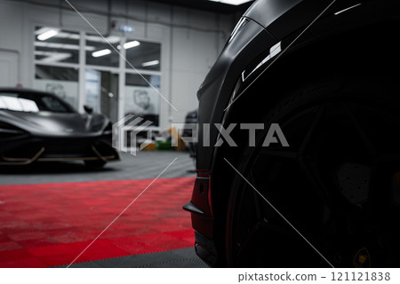 A close up view of a Lamborghini Urus Performante with a sleek black exterior. The McLaren 720S is partially visible in a well lit garage with a checkered floor. 121121838