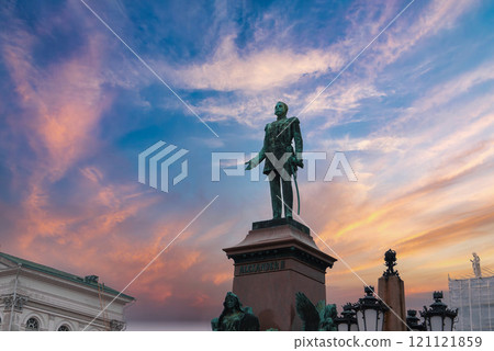 The statue of Alexander II stands in Senate Square, Helsinki, against a vibrant sunset sky. Helsinki Cathedral is partially visible on the left. 121121859