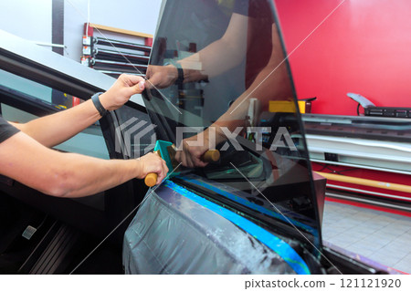 Technician applies window film to side of vehicle in an automotive workshop. 121121920