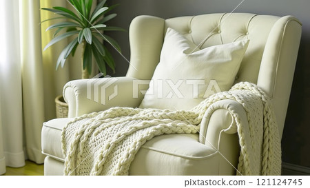 Cosy armchair with thick knitted plaid in light olive colour and cushion. Home decor in a romantic style. 121124745