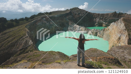 Woman enjoy volcano mountain crater edge. Volcanic Kelimutu blue crater lake. Travel destination. Beautiful wild landscape. Female tourist on summer vacation. Lifestyle holiday concept. Back view 121124910