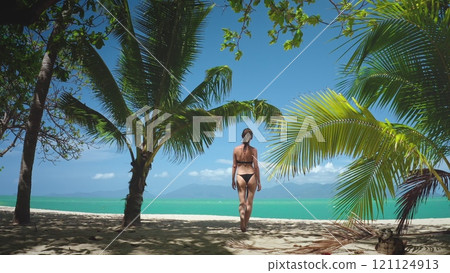 Beautiful woman relax tropical paradise beach on summer holiday vacation. Female in bikini walks along sandy beach in French Polynesia. Tall palm trees line shore, amazing exotic island wild nature. Beautiful woman relax tropical paradise beach on summer holiday vacation. Female in bikini walks along sandy beach in French Polynesia. Tall palm trees line shore, amazing exotic island wild nature. 121124913