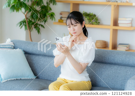 A young woman operating a smartphone in a room 121124928