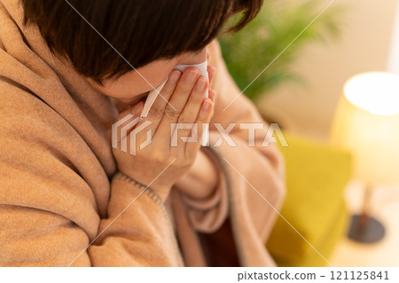 A middle-aged woman blowing her nose in the living room on a winter night 121125841
