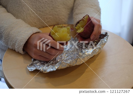 Elementary school student's hands splitting roasted sweet potatoes on a stove 121127267