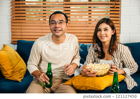 Excited young Asian couple husband and wife celebrate a football goal at home enhancing their leisure weekend with cheers excitement and togetherness as enthusiastic sports spectators. 121127450