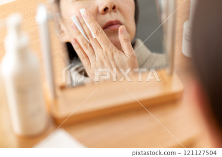 中高級女性在鏡子前使用基本化妝品進行皮膚護理 中高級女性在鏡子前使用基本化妝品進行皮膚護理 121127504