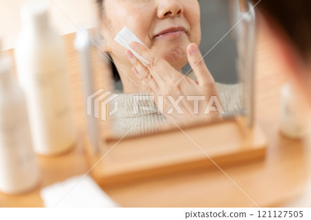 Middle-aged to senior women using skin care products in front of a mirror 121127505