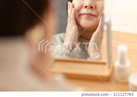 Middle-aged to senior women using skin care products in front of a mirror Middle-aged to senior women using skin care products in front of a mirror 121127765