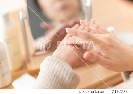 Middle-aged to senior women using skin care products in front of a mirror 121127821