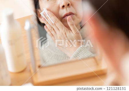 Middle-aged to senior women using skin care products in front of a mirror Middle-aged to senior women using skin care products in front of a mirror 121128131