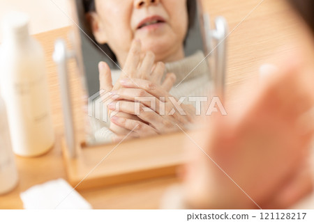 Middle-aged woman doing skin care for her hands in front of a mirror Middle-aged woman doing skin care for her hands in front of a mirror 121128217
