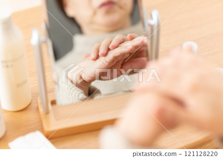 Middle-aged woman doing skin care for her hands in front of a mirror Middle-aged woman doing skin care for her hands in front of a mirror 121128220