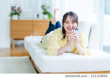 A young woman operating a smartphone in a room 121129608