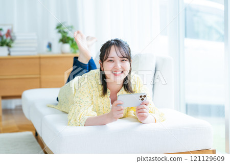A young woman operating a smartphone in a room 121129609