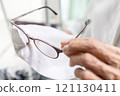 Close up of spectacles,hands of senior woman holding eyeglasses,old elderly cleaning the lenses of glasses with her shirt,using her clothes to wipe spectacles,cleans glasses from dust and dirt 121130411