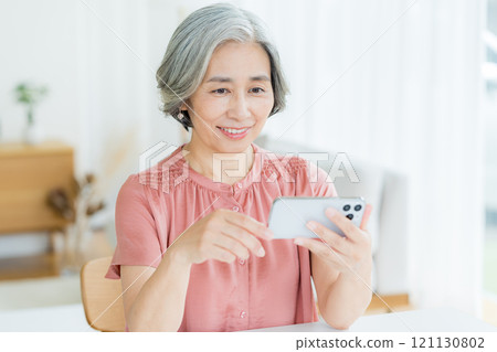Senior woman operating a smartphone in the living room 121130802