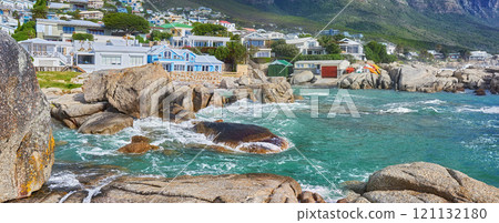 Scenic view of sea, rocks and residential buildings in Camps Bay Beach, Cape Town, South Africa. Tidal ocean waves washing over shoreline rocks and boulders. Overseas travel and tourism destination 121132180