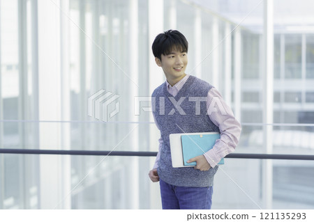 Portrait of a young man standing with a laptop and a notebook 121135293
