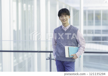 Portrait of a young man standing with a laptop and a notebook 121135294