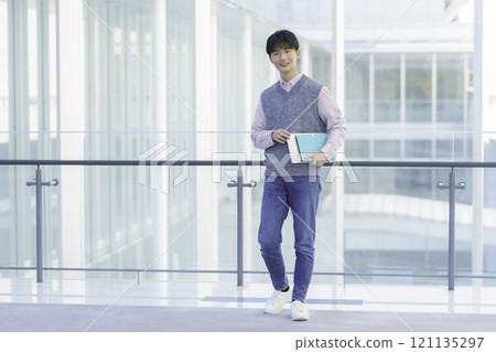 Portrait of a young man standing with a laptop and a notebook 121135297