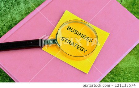 Business planning concept. BUSINESS STRATEGY on yellow paper through a magnifying glass close-up, top view 121135574