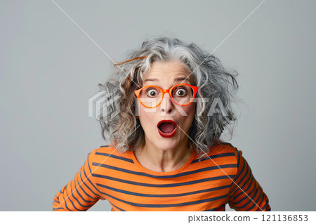 Joyful, very surprised 70 year old American woman with big amazed eyes and surprised mouth, with intense makeup, red lips, hair styling and red glasses. Live emotions. Idea for advertising. Banner 121136853