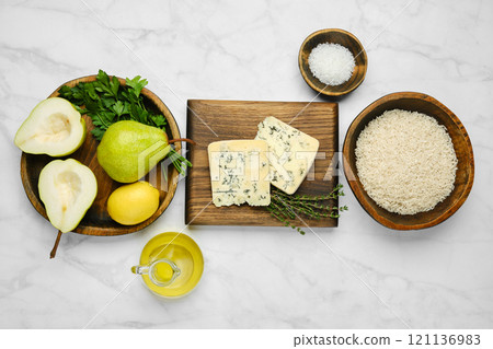 Overhead view of sliced pear, lemon, and parsley are alongside bowls of rice, blue mold cheese, salt, thyme, and olive oil on a marble countertop 121136983