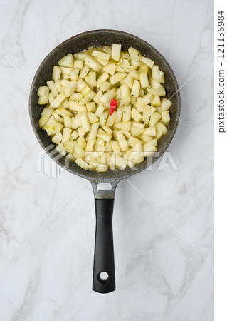 Cooking diced pears in a frying pan on a marble countertop in a warm kitchen setting 121136984