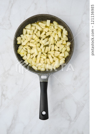Chopped green pears in a frying pan ready for cooking on a marble kitchen countertop 121136985