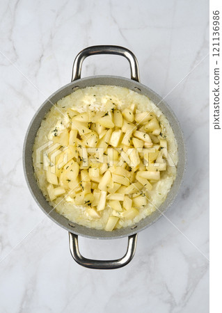 Creamy rice dish with diced pears and herbs in a silver pot on a marble countertop 121136986