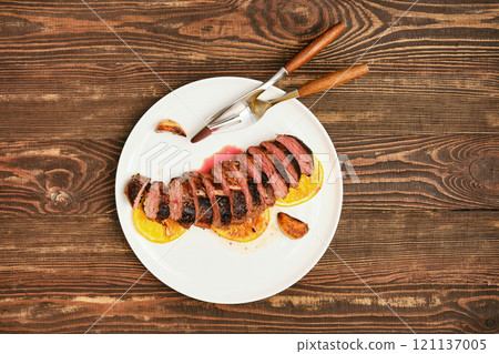 Juicy sliced dusk breast steak garnished with oranges on a rustic wooden table Juicy sliced dusk breast steak garnished with oranges on a rustic wooden table 121137005