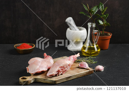 Fresh rabbit legs prepared for cooking with herbs and spices on a wooden cutting board Fresh rabbit legs prepared for cooking with herbs and spices on a wooden cutting board 121137010