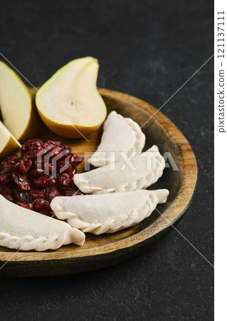 Delicious empanadas with cranberries and fresh pear on a wooden platter 121137111