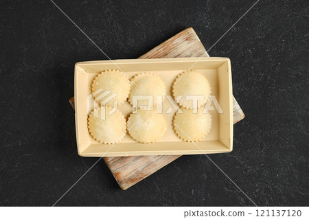 Homemade ravioli placed in a beige tray on a wooden cutting board in a kitchen setting 121137120