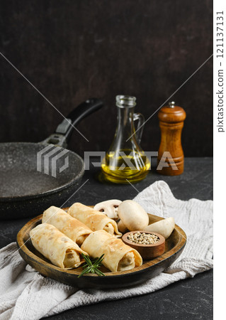 Delicious vegetarian crepes with mushrooms served on a wooden plate with cooking essentials nearby Delicious vegetarian crepes with mushrooms served on a wooden plate with cooking essentials nearby 121137131