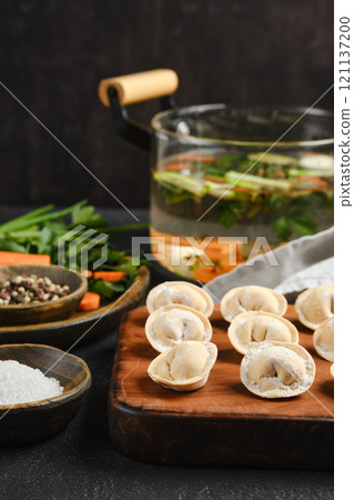 Dumplings arranged on a wooden board next to fresh herbs and boiling broth 121137200