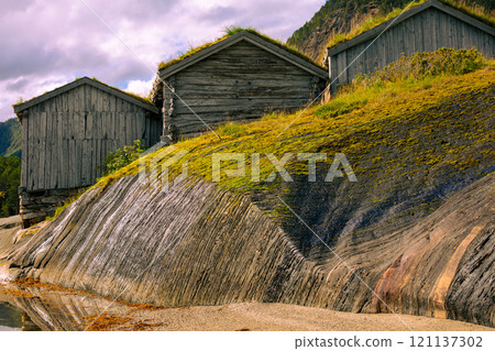 Old grunge wooden fishermen's house with green grass on roofs against fjord 121137302