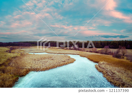 Aerial view of the countryside and frozen winding brook in the evening at sunset light. Beautiful nature landscape with cloudy sky Aerial view of the countryside and frozen winding brook in the evening at sunset light. Beautiful nature landscape with cloudy sky 121137390