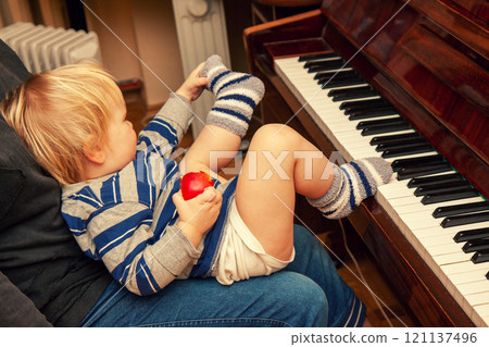 A little boy sits near the piano and plays with his feet 121137496